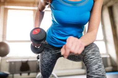 Spor salonunda dambıllarla egzersiz yapan bir kadın. Güç egzersizi. Fiziksel ve zihinsel sağlık için rutin egzersiz. Kuvvet egzersizi.