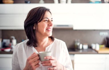 Mutfakta kahve içen güzel olgun bir kadın. Yaşlı kadın yalnız yaşıyor, huzurlu hafta sonunun tadını çıkarıyor..