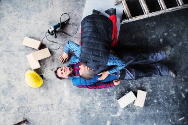İş arkadaşı kazadan sonra yerde yatan yaralı bir işçiye kalp masajı yapıyor. İş yerinde iş güvenliği ve sağlık kavramı.