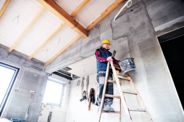 İnşaat işçisi merdivende duruyor, beton duvarda çalışıyor..