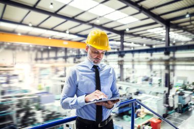 Portrait of project manager standing in modern industrial factory. Manufacturing facility with robotics, robotic arms and automation. clipart