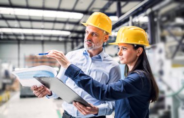 Modern endüstriyel fabrikada iki proje yöneticisi duruyor. Robot, robotik kollar ve otomasyon ile üretim tesisi.