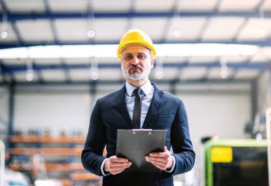 Modern endüstriyel fabrikada duran proje yöneticisinin portresi. Robot, robotik kollar ve otomasyon ile üretim tesisi.