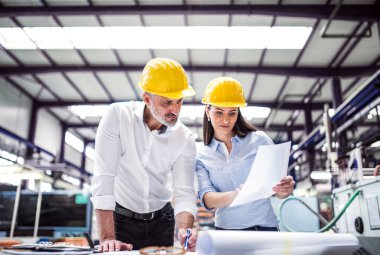 Modern endüstriyel fabrikada iki proje yöneticisi duruyor. Robot, robotik kollar ve otomasyon ile üretim tesisi.