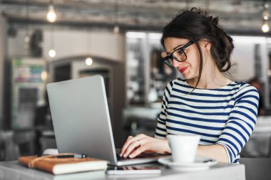 Kafede uzaktan çalışan bir kadın. Cappucino ve laptop masada. Kafede bir defter üzerinde çalışan serbest çalışan bir kadın..