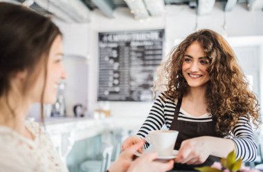 Kahve dükkanında çalışan güzel bir bayan barista bayan müşteriye kahve servisi yapıyor. Bir kafede yarı zamanlı çalışan üniversite öğrencisi..