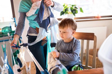 Küçük oğlu annesine ev işlerinde yardım ediyor, çamaşırları kurutma sehpasına asıyor. Haftalık ev işleri, aile için hafta sonu aktiviteleri.