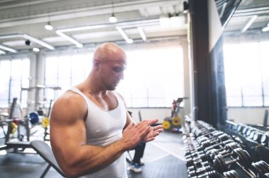 Spor salonunda egzersiz yapan güçlü bir adam avuçlarındaki tebeşire bakıyor. Fiziksel ve zihinsel sağlık için rutin egzersiz. Kapat..