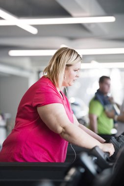 Spor salonunda koşu bandında egzersiz yapan kilolu bir kadın..