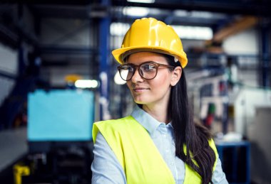 Modern endüstriyel fabrikada duran kadın proje yöneticisinin portresi. Robot, robotik kollar ve otomasyon ile üretim tesisi.