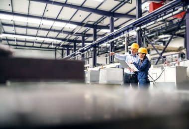 Modern endüstriyel fabrikada iki proje yöneticisi duruyor. Robot, robotik kollar ve otomasyon ile üretim tesisi.