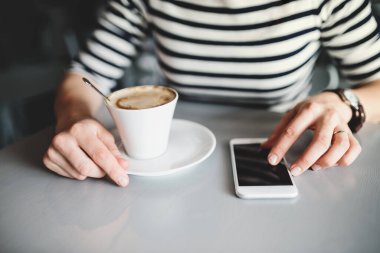 Cep telefonu kullanan ve kahvecide kahve içen mutlu genç bir kadın..