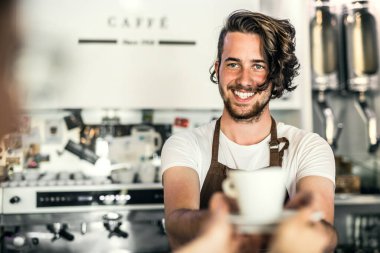 Kahve dükkanında çalışan yakışıklı barista, müşteriye kahve hazırlıyor. Bir kafede yarı zamanlı çalışan üniversite öğrencisi..