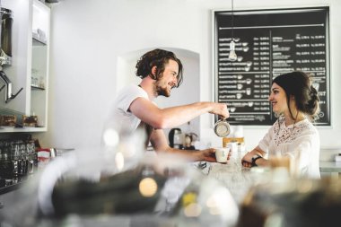 Barista kahvecide çalışıyor, bayan müşterilere servis yapıyor, kahve hazırlıyor. Kafede yarı zamanlı çalışan üniversite öğrencisi..