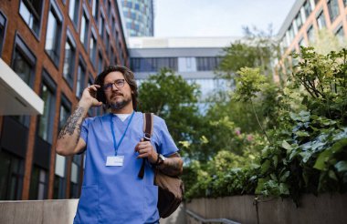 Üniformalı bir erkek doktor işten eve gidiyor, akıllı telefondan arıyor. Sağlık çalışanlarının iş-yaşam dengesi.