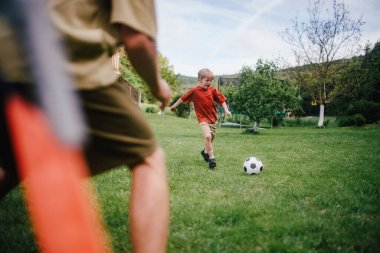 Babamın küçük oğluyla eğlenmesi, futbol oynaması, koşması ve top oynaması. Evlerinin önündeki çimenlikte oynuyorlar. Babalık ve Babalar Günü konsepti.