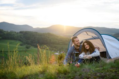 Gezginler, dışarıda çadır barınağında uyuyarak vakit geçiriyorlar. Genç turist doğada oturuyor, dinleniyor, günbatımının tadını çıkarıyor. Doğada romantik bir yaz tatili.