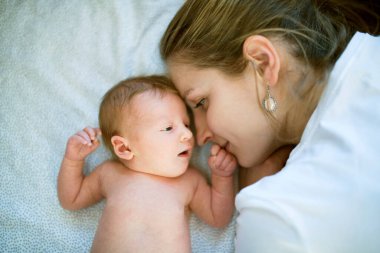 Yeni anne, yeni doğmuş bir bebeğin yanında yatıp ona bakıyor. Koşulsuz baba sevgisi, huzurlu aile anı.