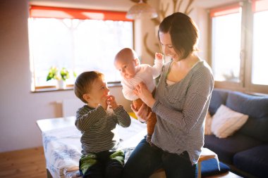 Mutlu anne kucağında küçük bir bebekle ağabeyiyle oynuyor, gülümsüyor. Koşulsuz baba sevgisi ve aile anı.