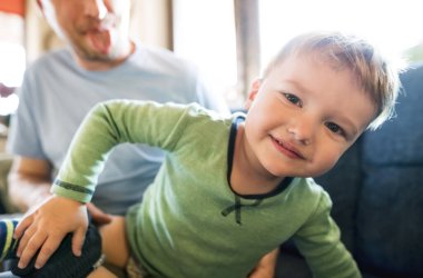 Baba, yeni yürümeye başlayan oğluna kıyafet giydirip gülmeye çalışıyor. Sıkı çalışma..