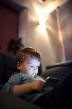 Tatlı çocuk yatakta oturup akıllı telefondan bir şeyler izliyor. Çocuklar için ekran saati..