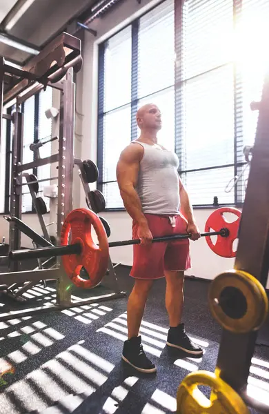 Kırmızı halterle kaldırma yapan güçlü bir adam. Fiziksel ve zihinsel sağlık için rutin çalışma.