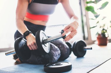 Güzel kızıl saçlı kadınlar dambılla evde egzersiz yapıyorlar. Oturma odasında spor salonu idmanı, spor kıyafetleri giyen bir kadın..