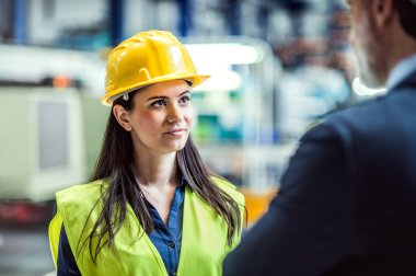 Depo çalışanı depoda lojistik çalışanıyla el sıkışıyor, ürünlerin, malların nakliyesini planlıyor, nakliye işlemleri hakkında konuşuyor. Ürünleri ve malzemeleri depoda depoluyor..