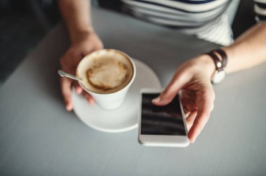 Cep telefonu kullanan ve kahvecide kahve içen mutlu genç bir kadın..