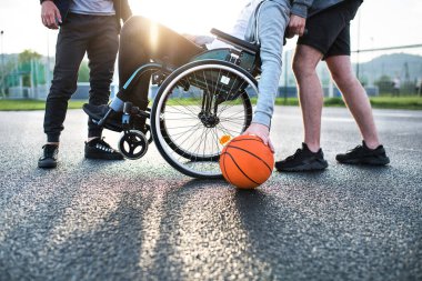 Tekerlekli sandalyede arkadaşlarıyla oyun alanında basketbol oynayan engelli bir genç. Takım çalışması ve erkek arkadaşlığı.