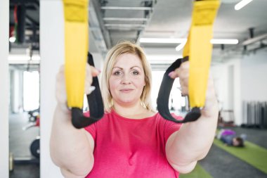 Kilolu bir kadın spor salonunda egzersiz yapıyor, uzaklaştırma eğitimi alıyor, tamamen direnç egzersizi yapıyor. Kişisel antrenör onu çalıştırıyor ve ona yardım ediyor.