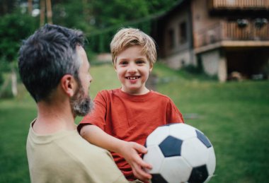 Babamın küçük oğluyla eğlenmesi, futbol oynaması, koşması ve birbirini yakalaması. Evlerinin önündeki çimenlikte oynuyorlar. Babalık ve Babalar Günü konsepti.