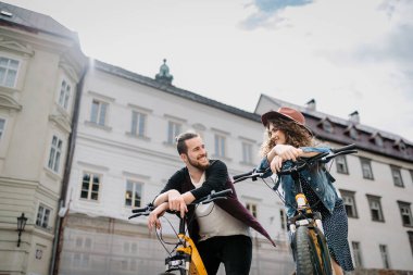 Elektrikli scooterlı bir çift gezgin, şehir turu. Yaz tatillerinde bisiklet kullanan genç turistler..