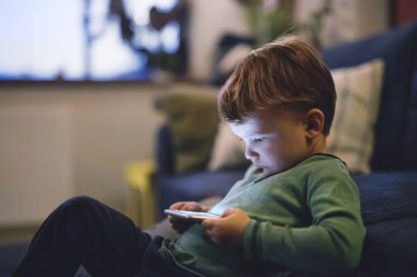 Tatlı çocuk yatakta oturup akıllı telefondan bir şeyler izliyor. Çocuklar için ekran saati..