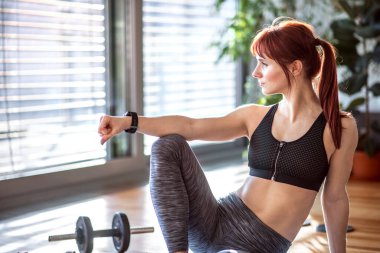 Spor yaparken güzel kızıl saçlı kadının vesikalığı. Oturma odasında spor salonundaki spor salonunda spor kıyafetleri giyen bir kadın..