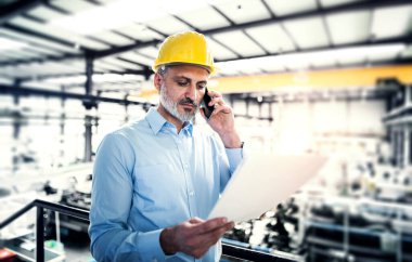 Proje yöneticisinin portresi modern endüstriyel fabrikada duruyor, telefon görüşmesi yapıyor. Robot, robotik kollar ve otomasyon ile üretim tesisi.