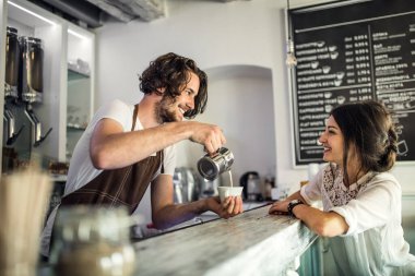 Kahve dükkanında çalışan yakışıklı barista tezgahtaki bayan müşteriye kahve hazırlıyor. Bir kafede yarı zamanlı çalışan üniversite öğrencisi..