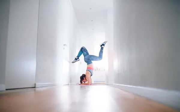 stock image Beautiful redhead woman doing headstand during home fitness routine. Home workout on gym mt in living room, sporty woman wearing sportswear. Minimalistic shot.