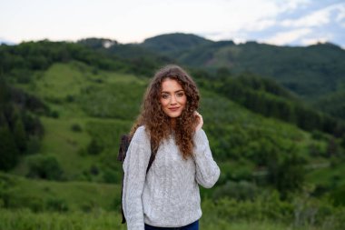 Sırt çantalı güzel bir turist kadın gezgin doğa yürüyüşü yapıyor. Dağlarda yürüyüş yapan aktif yürüyüşçü gün batımının tadını çıkarıyor. Tek başına yaz tatili.