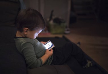 Tatlı çocuk yatakta oturup akıllı telefondan bir şeyler izliyor. Çocuklar için ekran saati..