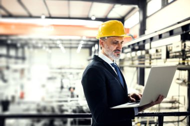 Modern endüstriyel fabrikada elinde not defteriyle duran proje yöneticisinin portresi. Robot, robotik kollar ve otomasyon ile üretim tesisi.