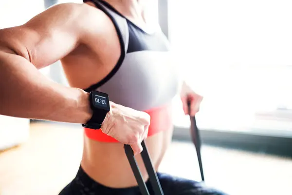 stock image Womans home fitness routine with resistance band. Home workout on gym mat in living room, sporty woman wearing sportswear clothes. Close up on arms