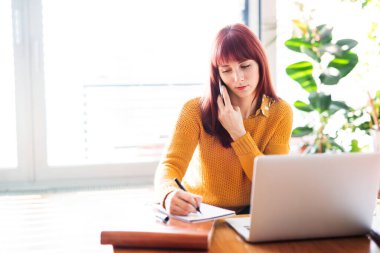 Mutfak adasında oturan kızıl saçlı kadın ev ofisinden laptopla arama yapıyor. Şehirdeki dairesinden uzaktan çalışan iş kadını..