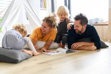Genç bir nükleer aile oturma odasında oyuncaklarla oynuyor. Ebeveynler ve çocuklar yerde yatar, çocuk hikayelerine, resimli kitaplara bakar, hafta sonunu evde geçirirler..