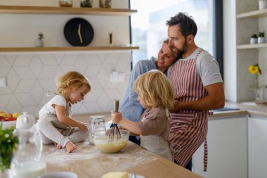 Nükleer aile birlikte krep yapıyor. Ebeveynler ve çocuklar mutfakta, krep hamuru hazırlıyorlar, hafta sonunu evde geçiriyorlar..