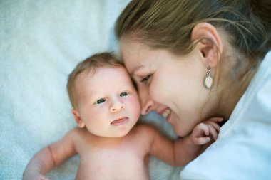 Yeni anne, yeni doğmuş bir bebeğin yanında yatıp ona bakıyor. Koşulsuz baba sevgisi, huzurlu aile anı.