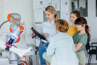 Gerçek robotik laboratuvarına saha gezisi, robotik kariyerinde çocukları cesaretlendiriyor. Gerçek bilim adamı genç öğrencilerle konuşuyor, onlara robotik bir kol gösteriyor..