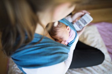 Yeni doğmuş bebek bebek askıda uyuyor, sarılıyor, annesi akıllı telefondan kayıyor. Koşulsuz baba sevgisi, anneler günü konsepti..