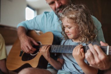 Baba ve oğul birlikte gitar çalıyorlar. Çocuklar müzik aletleriyle çalmayı ebeveynlerinden öğreniyorlar, baba..