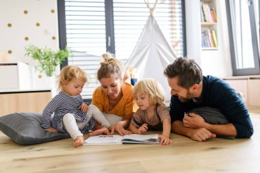 Genç bir nükleer aile oturma odasında oyuncaklarla oynuyor. Ebeveynler ve çocuklar yerde yatar, çocuk hikayelerine, resimli kitaplara bakar, hafta sonunu evde geçirirler..
